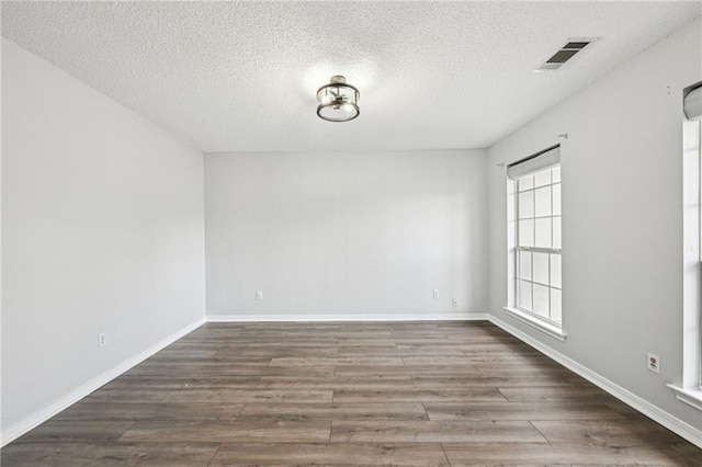 spare room with baseboards, a textured ceiling, visible vents, and wood finished floors