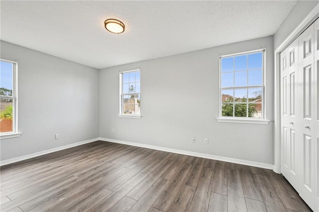 unfurnished bedroom featuring a textured ceiling, baseboards, dark wood finished floors, and a closet