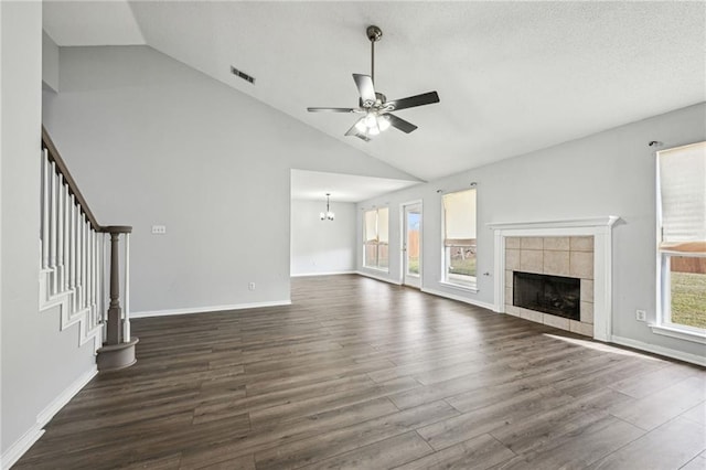 unfurnished living room featuring a fireplace, stairway, dark wood finished floors, and ceiling fan with notable chandelier