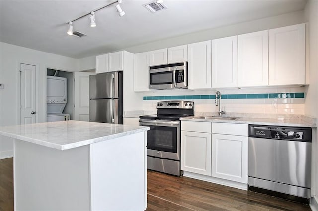 kitchen featuring sink, stacked washer / dryer, a kitchen island, stainless steel appliances, and white cabinets