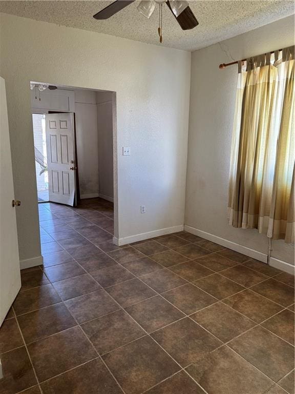 spare room featuring ceiling fan, dark tile patterned floors, and a textured ceiling