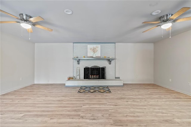 unfurnished living room with ceiling fan, a brick fireplace, and light hardwood / wood-style floors