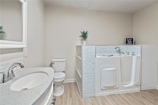 bathroom with tasteful backsplash, hardwood / wood-style flooring, vanity, a washtub, and toilet