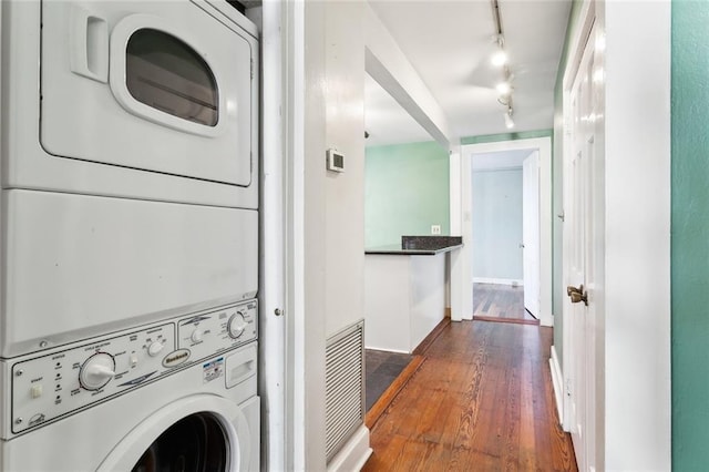 laundry area featuring stacked washer and clothes dryer, dark wood-type flooring, and track lighting