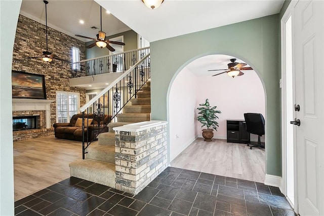 foyer entrance featuring a brick fireplace, a towering ceiling, wood-type flooring, and ceiling fan