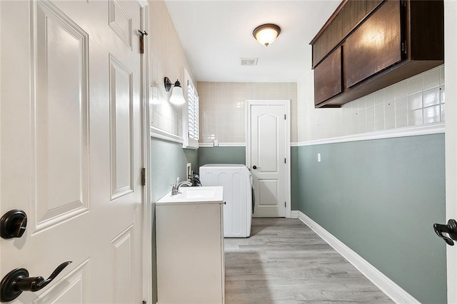 clothes washing area featuring cabinets, sink, washer / clothes dryer, and light hardwood / wood-style floors