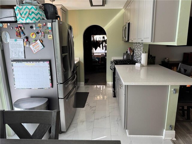 kitchen with gray cabinets, a kitchen breakfast bar, stainless steel appliances, tasteful backsplash, and kitchen peninsula