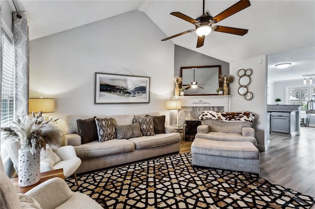 living room featuring ceiling fan, wood-type flooring, a tiled fireplace, and high vaulted ceiling