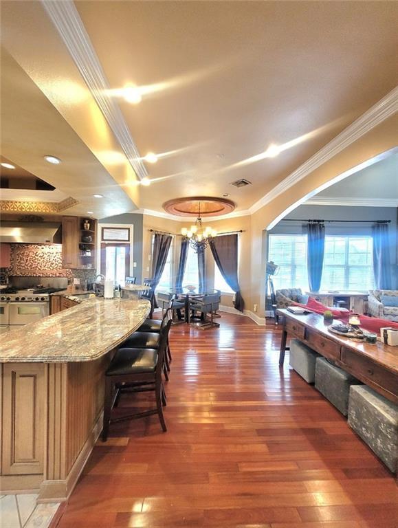 interior space with extractor fan, an inviting chandelier, light stone counters, crown molding, and dark hardwood / wood-style floors