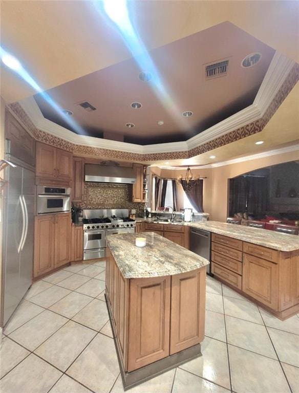 kitchen with premium appliances, a raised ceiling, kitchen peninsula, and a kitchen island