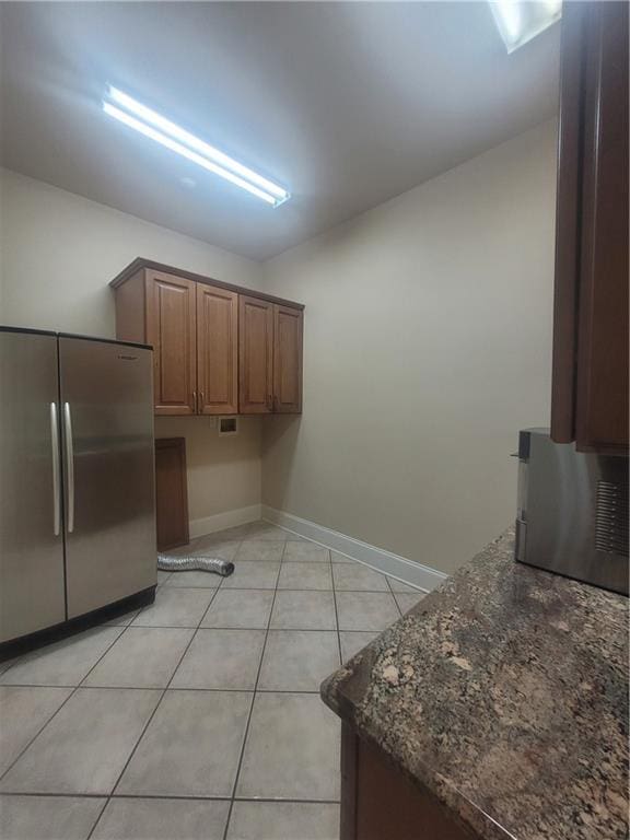 kitchen featuring light tile patterned floors, stainless steel fridge, and dark stone counters