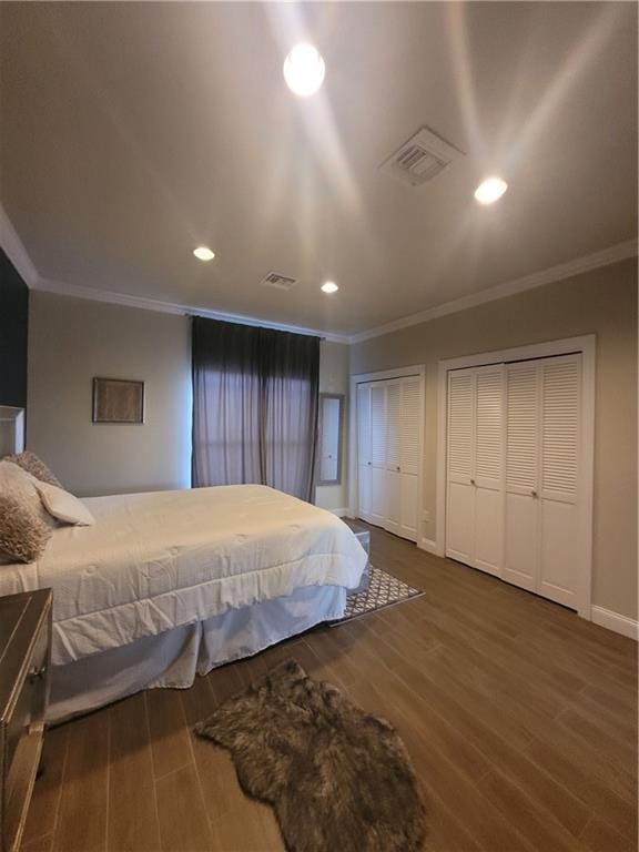 bedroom featuring crown molding, dark wood-type flooring, and two closets