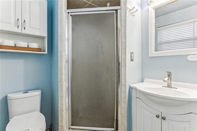 bathroom featuring a shower with door, vanity, and toilet