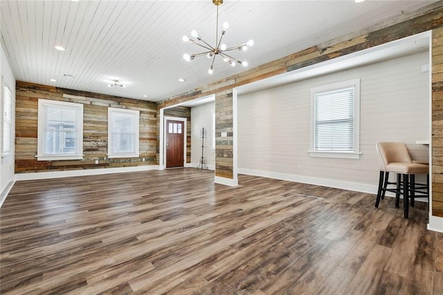 unfurnished living room with a notable chandelier, wood ceiling, plenty of natural light, and dark hardwood / wood-style floors