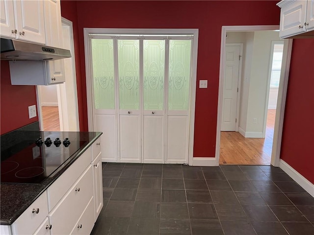 kitchen with black electric stovetop, dark stone counters, and white cabinets