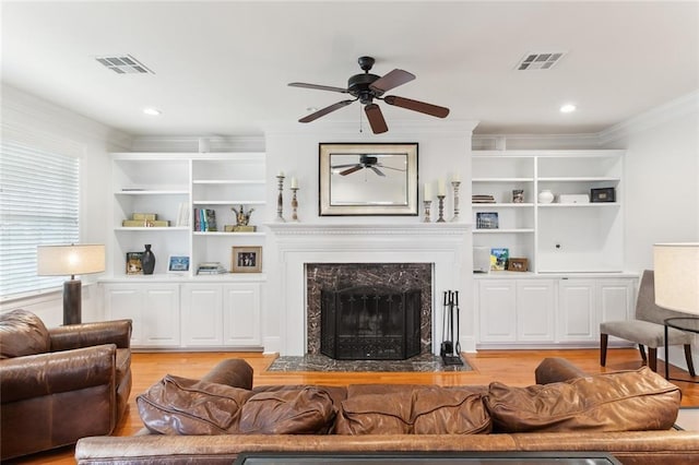 living room featuring a premium fireplace, light hardwood / wood-style floors, ceiling fan, built in features, and crown molding