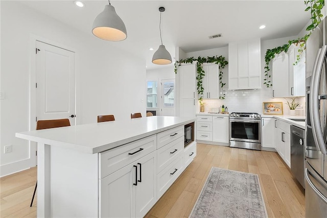 kitchen featuring stainless steel appliances, white cabinetry, a breakfast bar, and decorative light fixtures