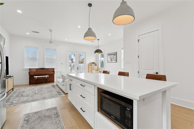 kitchen with a kitchen island, pendant lighting, white cabinets, and light hardwood / wood-style flooring