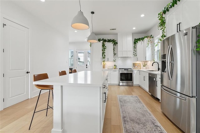 kitchen featuring pendant lighting, a breakfast bar area, white cabinetry, stainless steel appliances, and a kitchen island