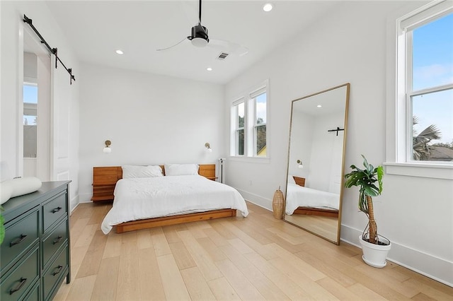 bedroom with a barn door, ceiling fan, and light wood-type flooring