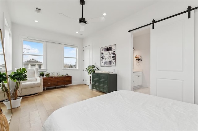 bedroom featuring connected bathroom, a barn door, ceiling fan, and light wood-type flooring