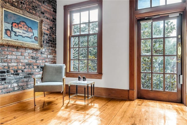 sitting room with light hardwood / wood-style flooring, a healthy amount of sunlight, and brick wall