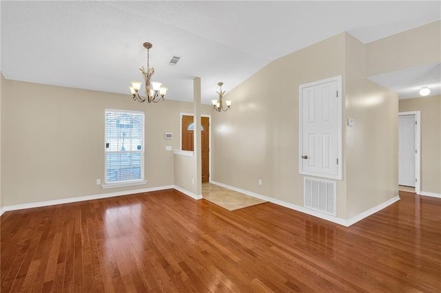 empty room with hardwood / wood-style flooring, vaulted ceiling, and an inviting chandelier