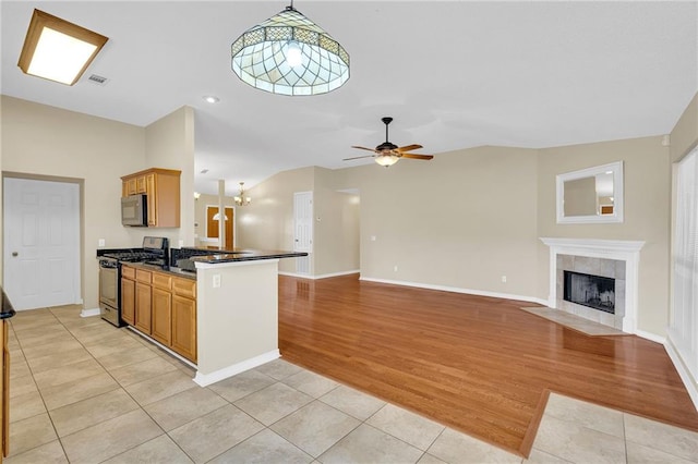 kitchen featuring light tile patterned floors, a tile fireplace, appliances with stainless steel finishes, decorative light fixtures, and kitchen peninsula