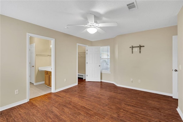 unfurnished bedroom with ceiling fan, ensuite bathroom, wood-type flooring, a walk in closet, and a closet