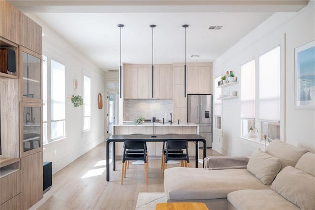 kitchen featuring stainless steel refrigerator with ice dispenser, sink, decorative light fixtures, light wood-type flooring, and backsplash