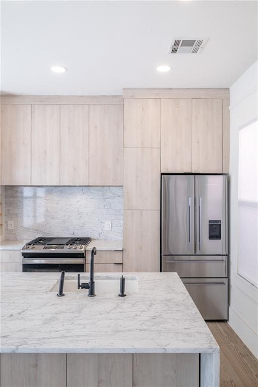 kitchen with appliances with stainless steel finishes, sink, backsplash, light hardwood / wood-style floors, and light brown cabinets