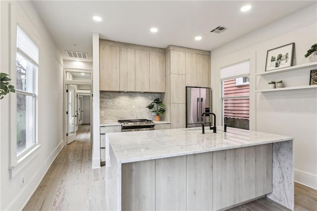 kitchen featuring a kitchen island with sink, light wood-type flooring, light stone countertops, and appliances with stainless steel finishes