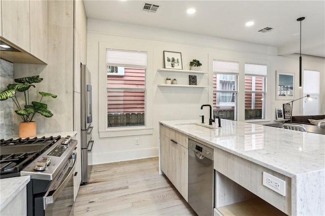 kitchen featuring sink, light stone counters, hanging light fixtures, light hardwood / wood-style flooring, and stainless steel appliances