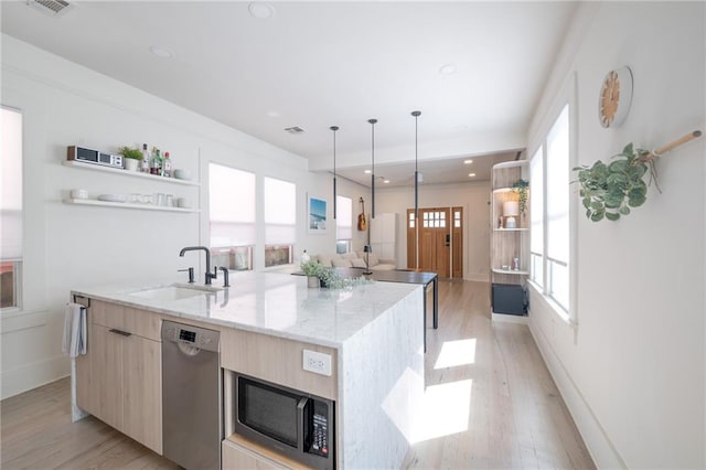 kitchen with light brown cabinetry, an island with sink, sink, light stone counters, and stainless steel appliances