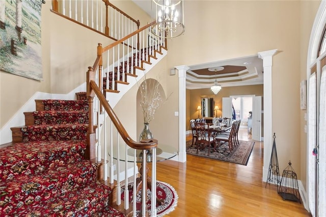 stairway with ornate columns, crown molding, a chandelier, a tray ceiling, and hardwood / wood-style flooring