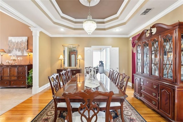 dining room with decorative columns, ornamental molding, light hardwood / wood-style floors, and a tray ceiling