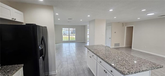 kitchen featuring white cabinetry, black fridge with ice dispenser, light stone countertops, and a kitchen island