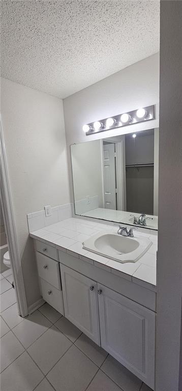 bathroom featuring tile patterned flooring, vanity, a textured ceiling, and toilet