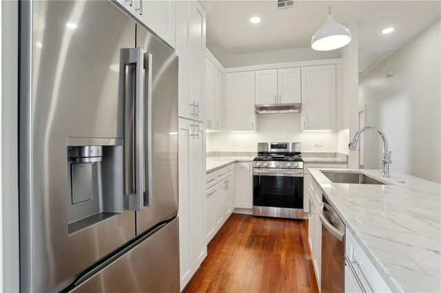 kitchen featuring sink, white cabinetry, stainless steel appliances, light stone countertops, and decorative light fixtures