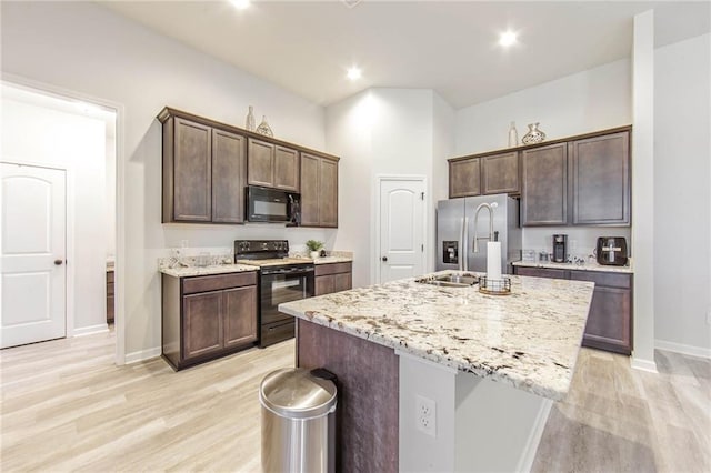 kitchen with dark brown cabinetry, light stone counters, black appliances, a center island with sink, and light wood-type flooring