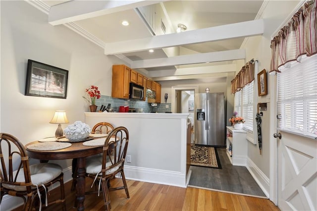 kitchen with vaulted ceiling with beams, tasteful backsplash, crown molding, appliances with stainless steel finishes, and hardwood / wood-style flooring