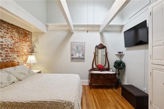 bedroom with brick wall, beamed ceiling, and light wood-type flooring