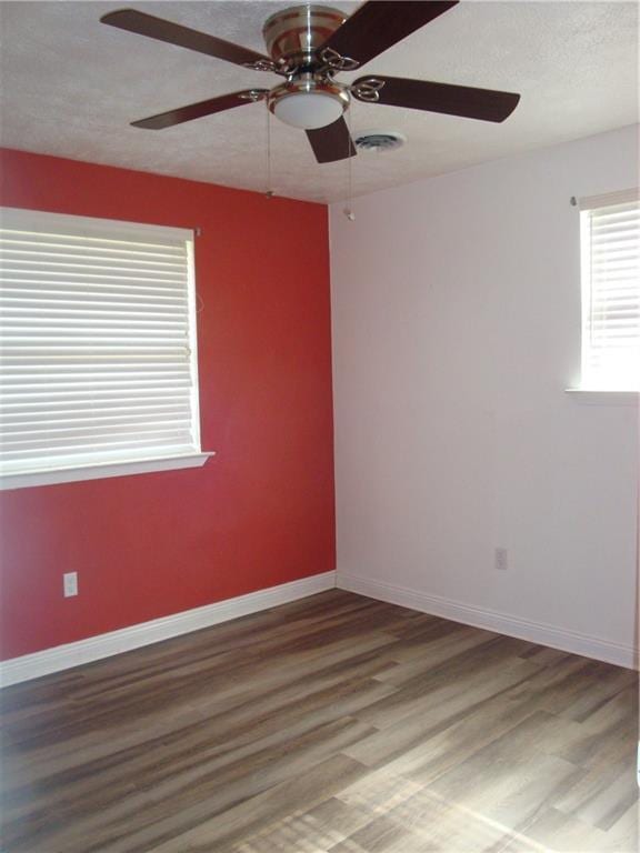 spare room with a textured ceiling, wood finished floors, visible vents, and baseboards