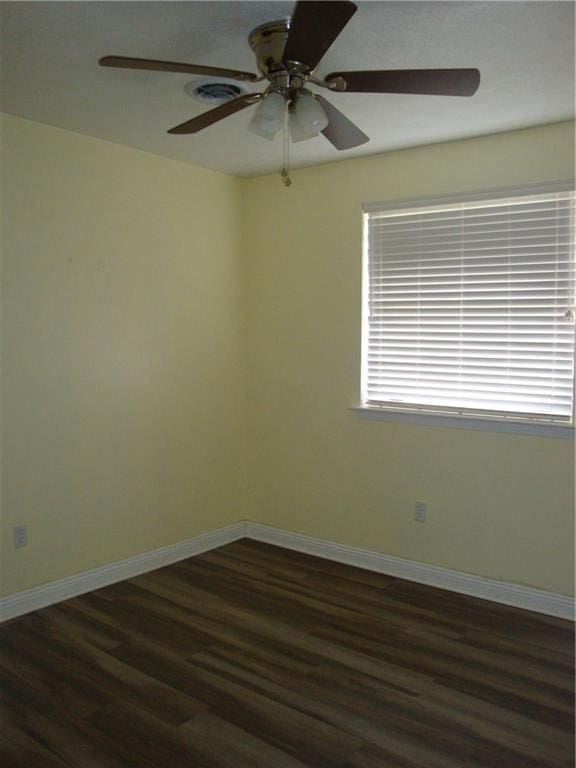 empty room featuring dark wood-type flooring, a ceiling fan, and baseboards