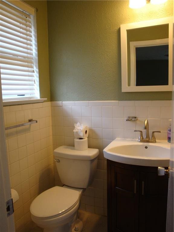 half bathroom with wainscoting, a textured wall, vanity, and toilet