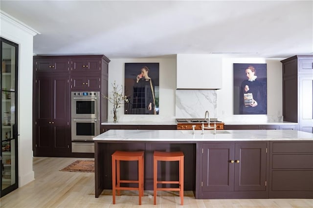 kitchen featuring a kitchen island, tasteful backsplash, sink, stainless steel double oven, and light hardwood / wood-style flooring