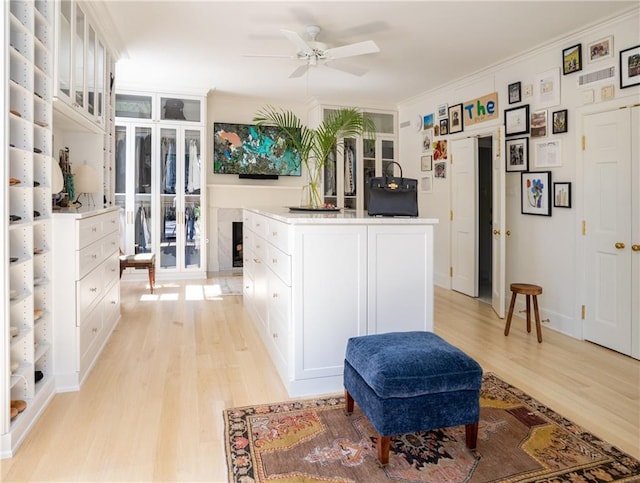 kitchen with an island with sink, white cabinets, crown molding, and light hardwood / wood-style flooring