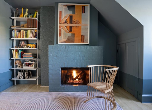 sitting room with wood-type flooring, vaulted ceiling, and a brick fireplace