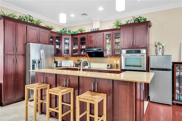 kitchen featuring a breakfast bar, ornamental molding, appliances with stainless steel finishes, pendant lighting, and a kitchen island with sink