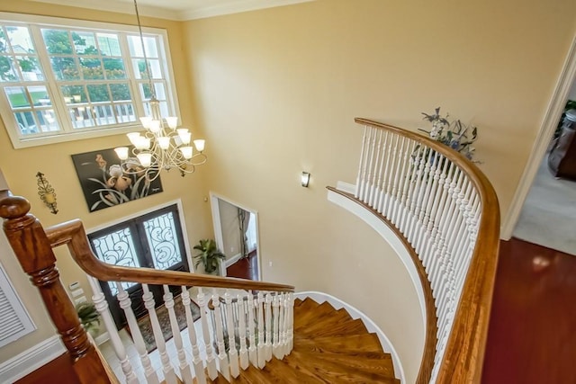 staircase featuring french doors, wood-type flooring, ornamental molding, a notable chandelier, and a towering ceiling